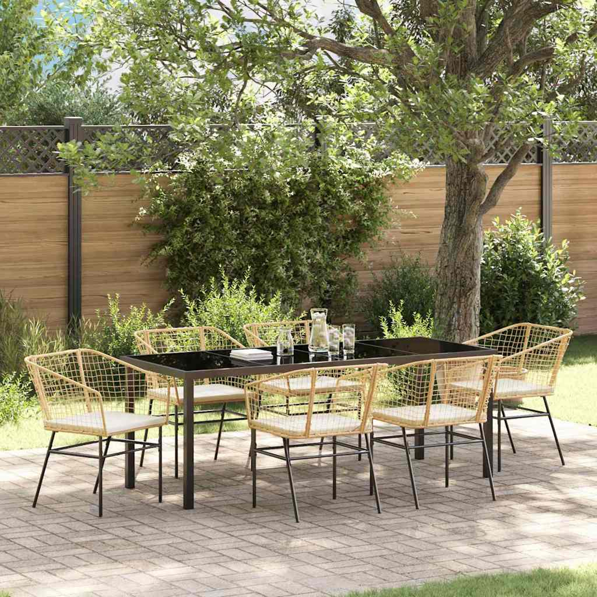 Essgruppe im Freien: schwarzer Tisch, Korbstühle, Gläser und eine Kanne. Auf einer Ziegelterrasse mit Grün und Bäumen im Hintergrund.