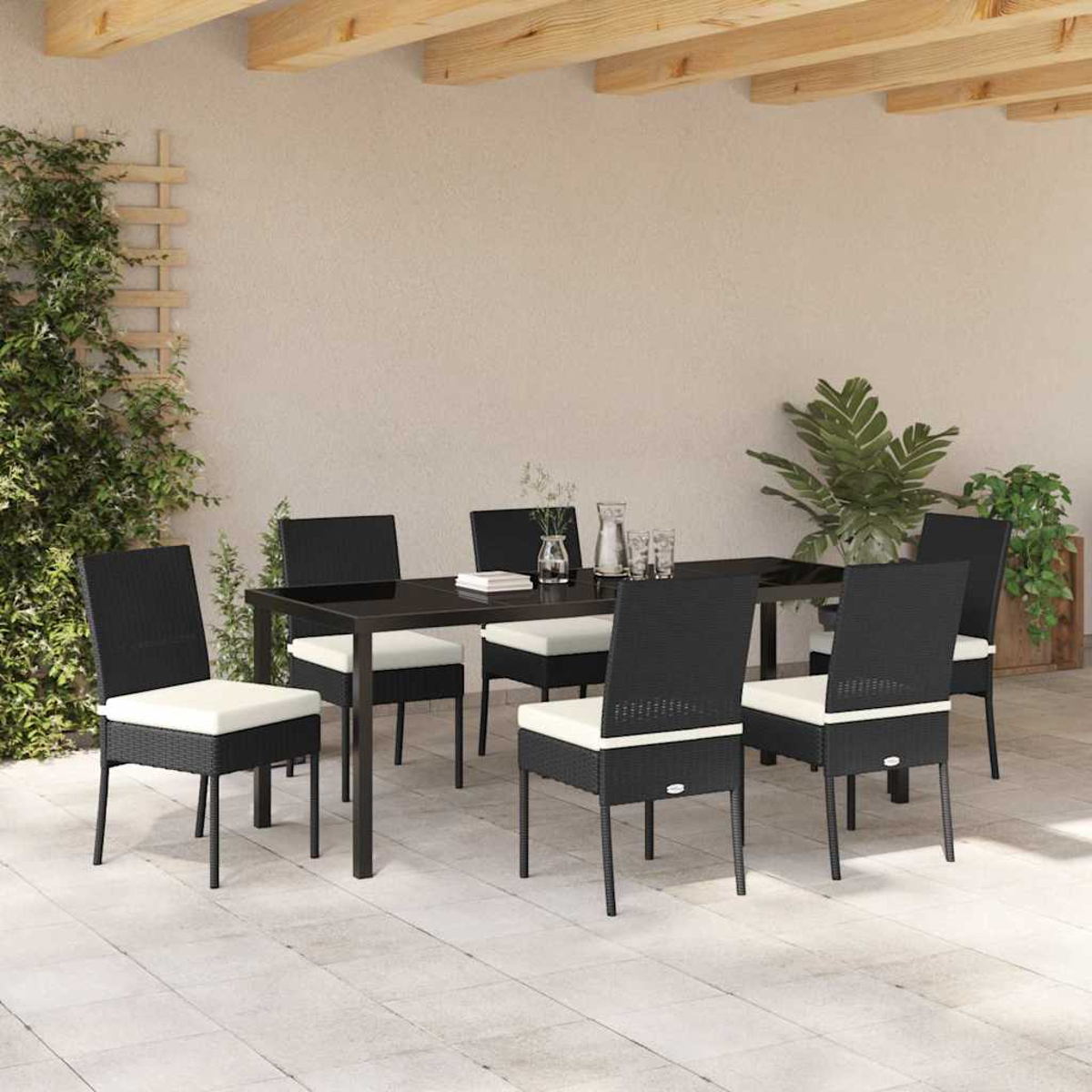 Essgruppe im Freien. Schwarze Stühle mit weißen Kissen umrunden einen schwarzen Tisch. Pflanzen sind im Hintergrund.