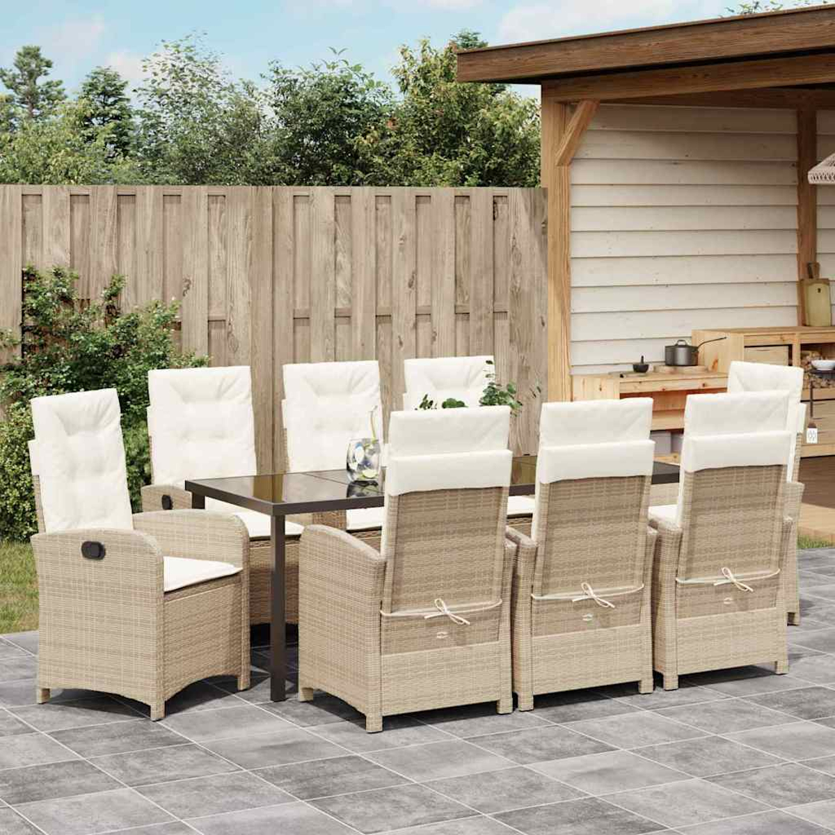 Essgruppe im Freien. Rattan-Stühle mit weißen Kissen umrunden einen schwarzen Tisch. Holzzaun und Schuppen im Hintergrund.
