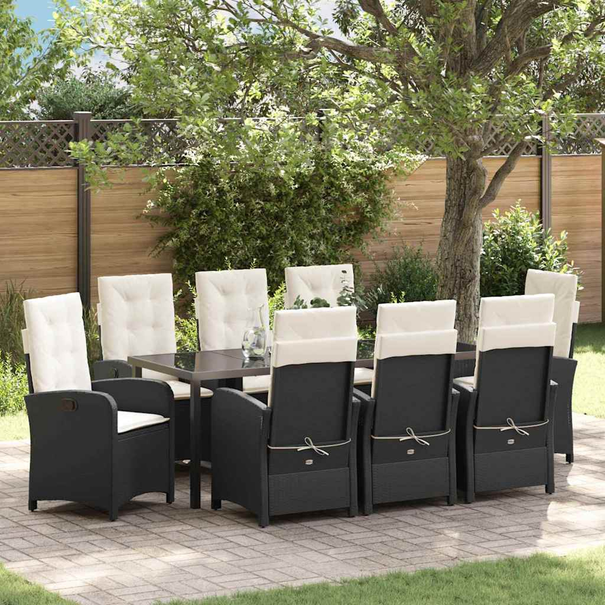 Essgruppe im Freien. Schwarze Stühle mit weißen Kissen umrunden einen Tisch auf der Terrasse. Grünes Laub und Holzzaun im Hintergrund.