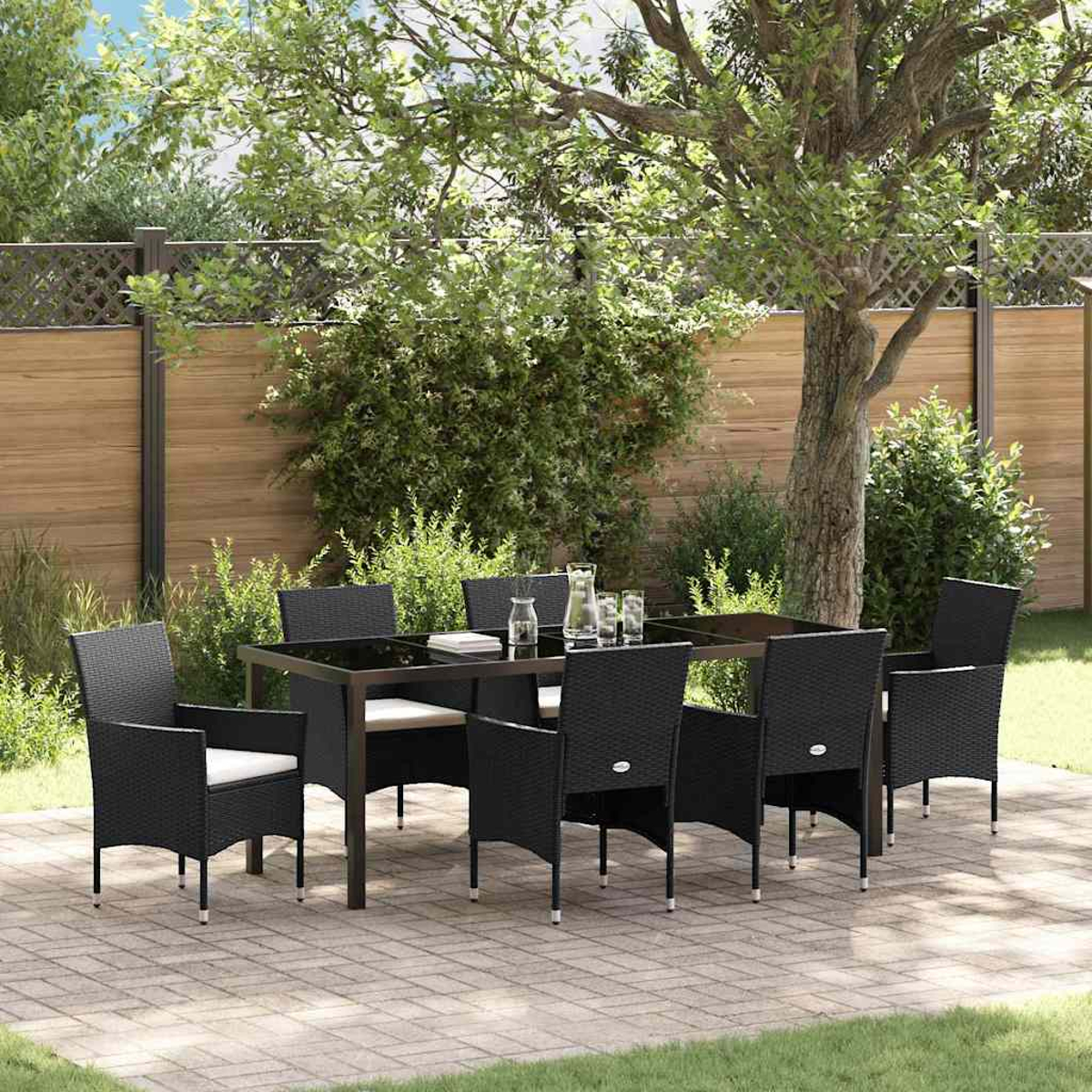 Set da pranzo all'aperto con sedie nere e tavolo in vetro. La scena è ambientata su un patio con una recinzione in legno e vegetazione lussureggiante.