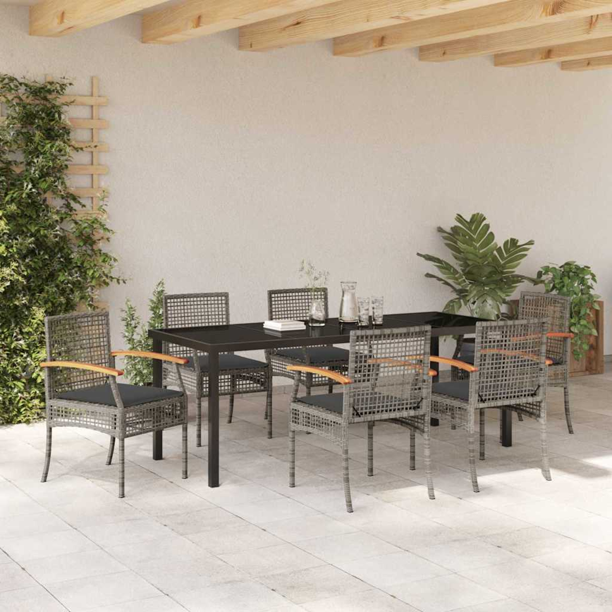 Eine Terrasse mit einem schwarzen Tisch, grauen Stühlen und Pflanzen. Holzbalken über Kopf und eine weiße Wand im Hintergrund.
