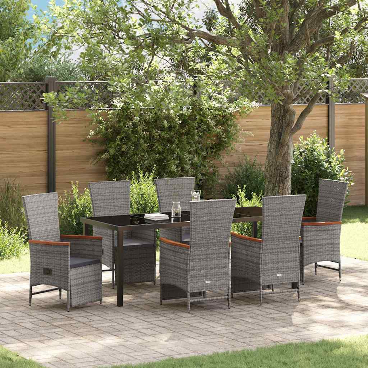Essgruppe im Freien: Tisch und sechs graue Korbstühle mit Holzarmlehnen, auf einer gepflasterten Terrasse, unter einem Baum.