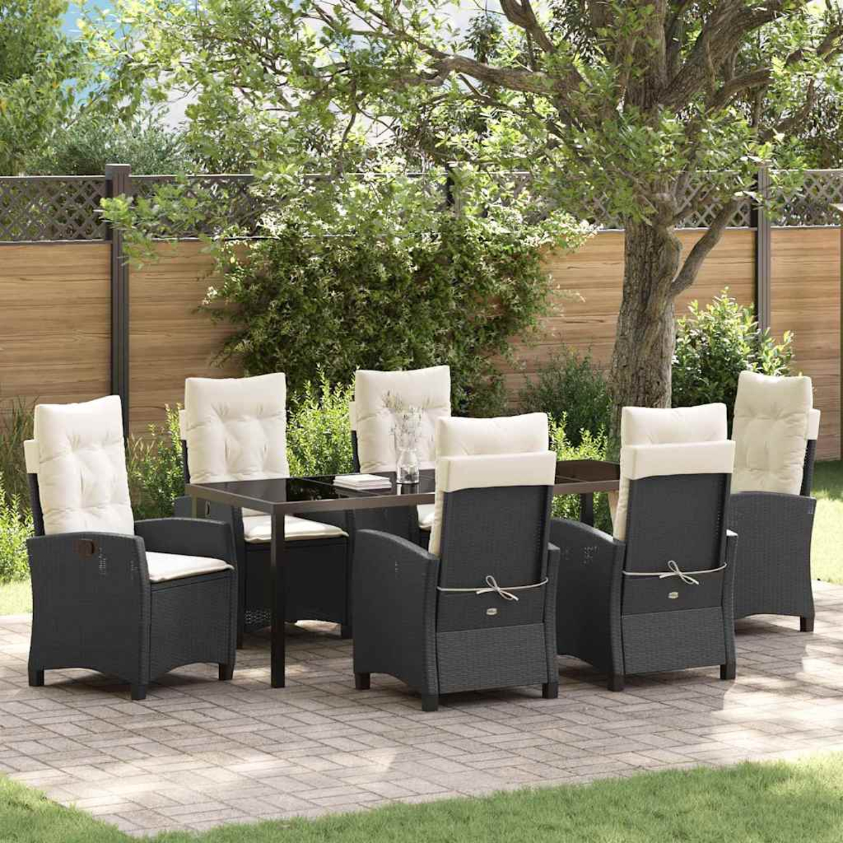 Set da pranzo all'aperto. Sedie in vimini nero con cuscini color crema attorno a un tavolo di vetro. Il giardino ha alberi e una staccionata in legno.