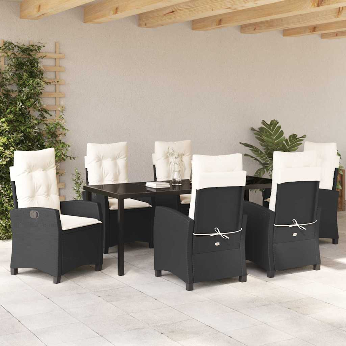 Set da pranzo all'aperto con sedie nere e cuscini bianchi attorno a un tavolo scuro. Piante verdi e travi di legno sopra.