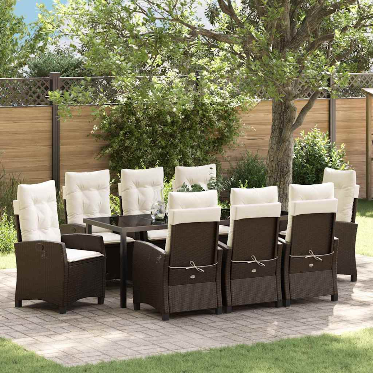 Set da pranzo all'aperto con sedie in vimini marrone, cuscini bianchi e un tavolo nero su un patio, con alberi e una recinzione sullo sfondo.
