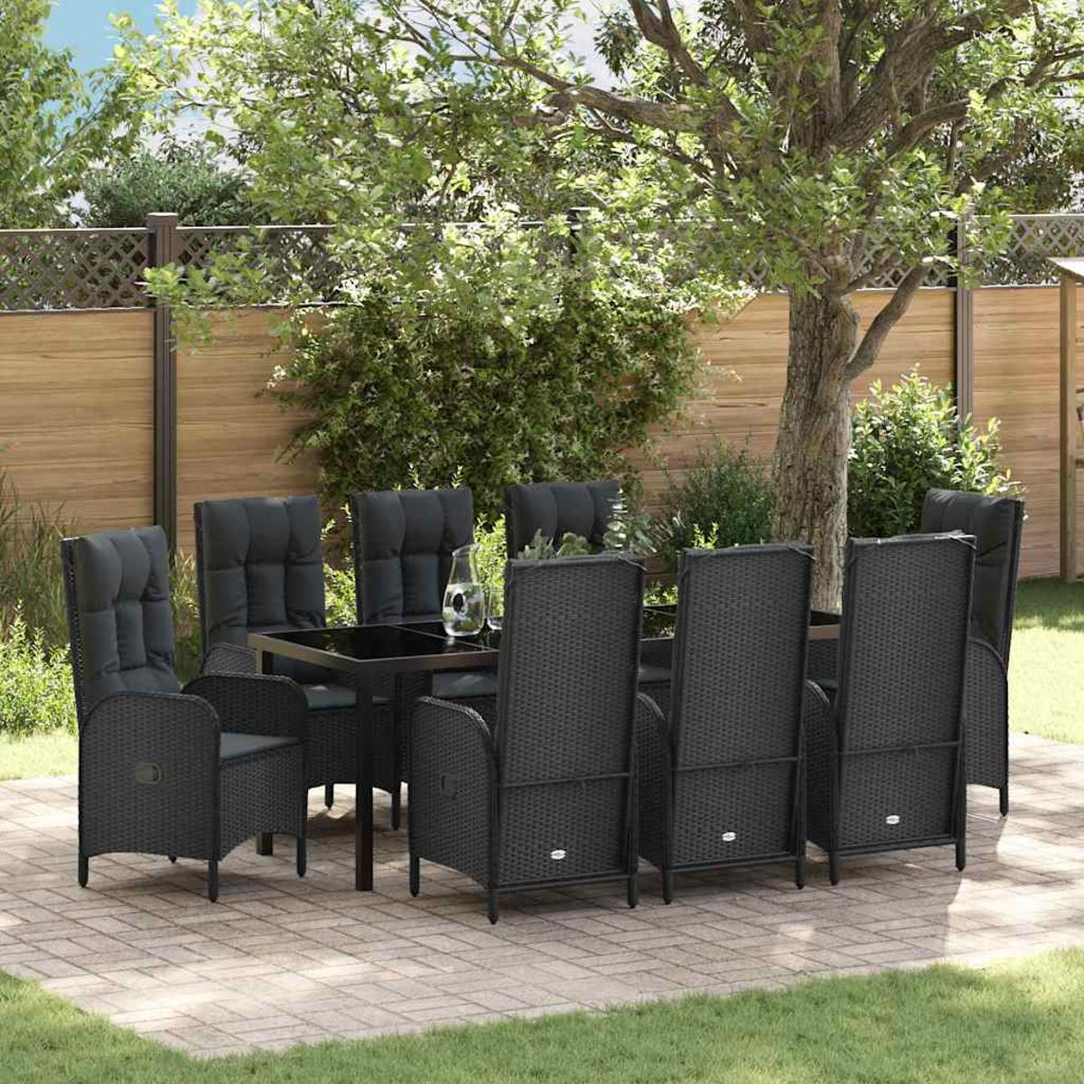 Essgruppe im Freien. Schwarze Korbstühle umrunden einen schwarzen Tisch auf einer Ziegelterrasse. Baum und Zaun im Hintergrund.