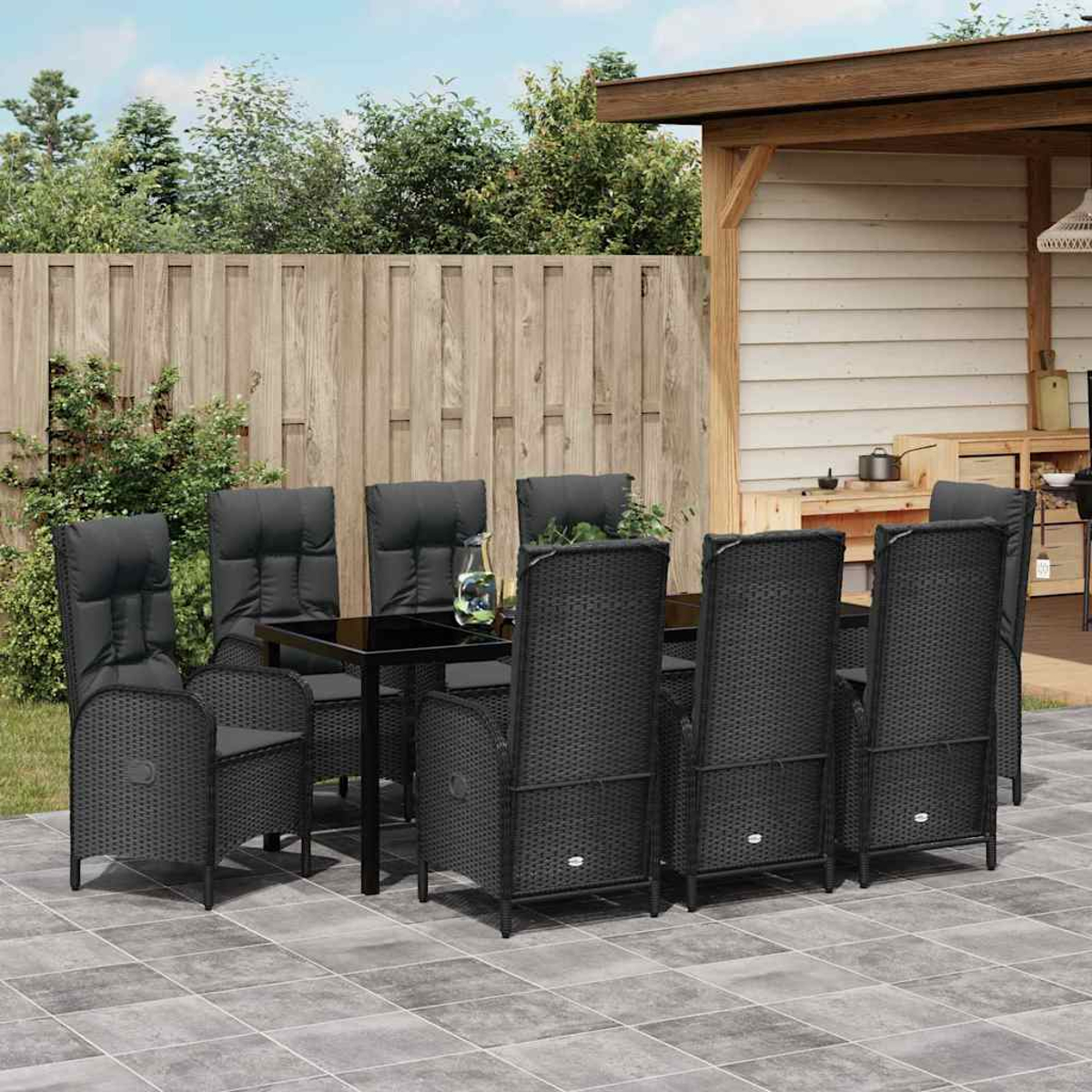 Essgruppe im Freien. Schwarze Korbstühle umgeben einen schwarzen Tisch auf einer gefliesten Terrasse. Holzzaun und -struktur im Hintergrund.
