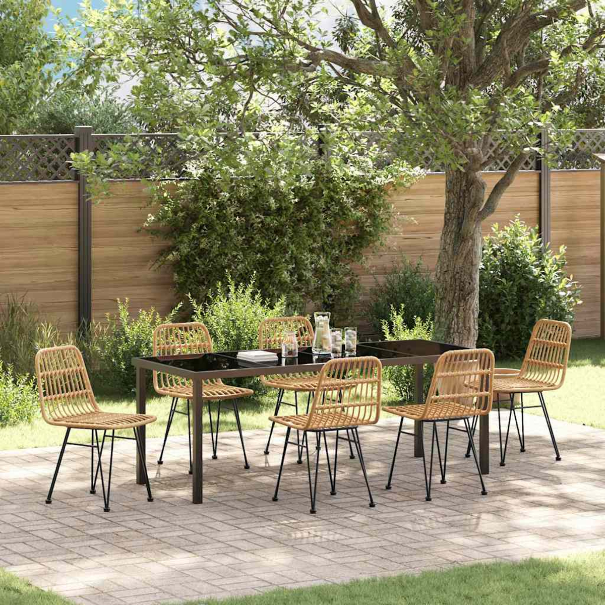 Set da pranzo all'aperto con tavolo nero e sedie in vimini su un patio in mattoni. Un albero e una recinzione sullo sfondo.
