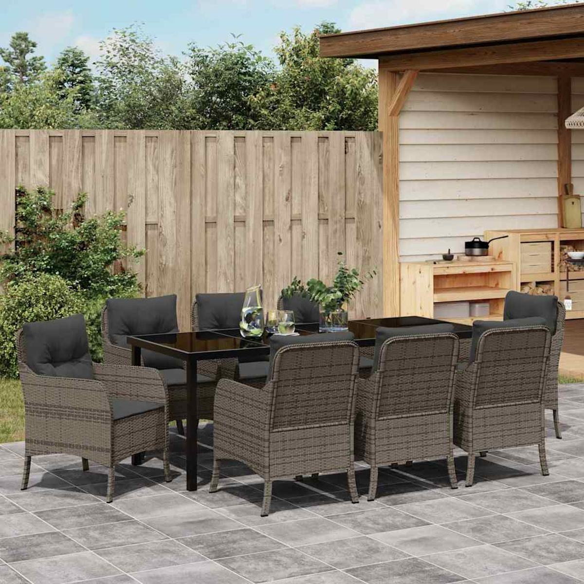 Essgruppe im Freien mit Tisch mit Glasplatte und Korbstühlen auf einer Terrasse. Holzzaun und Struktur im Hintergrund.