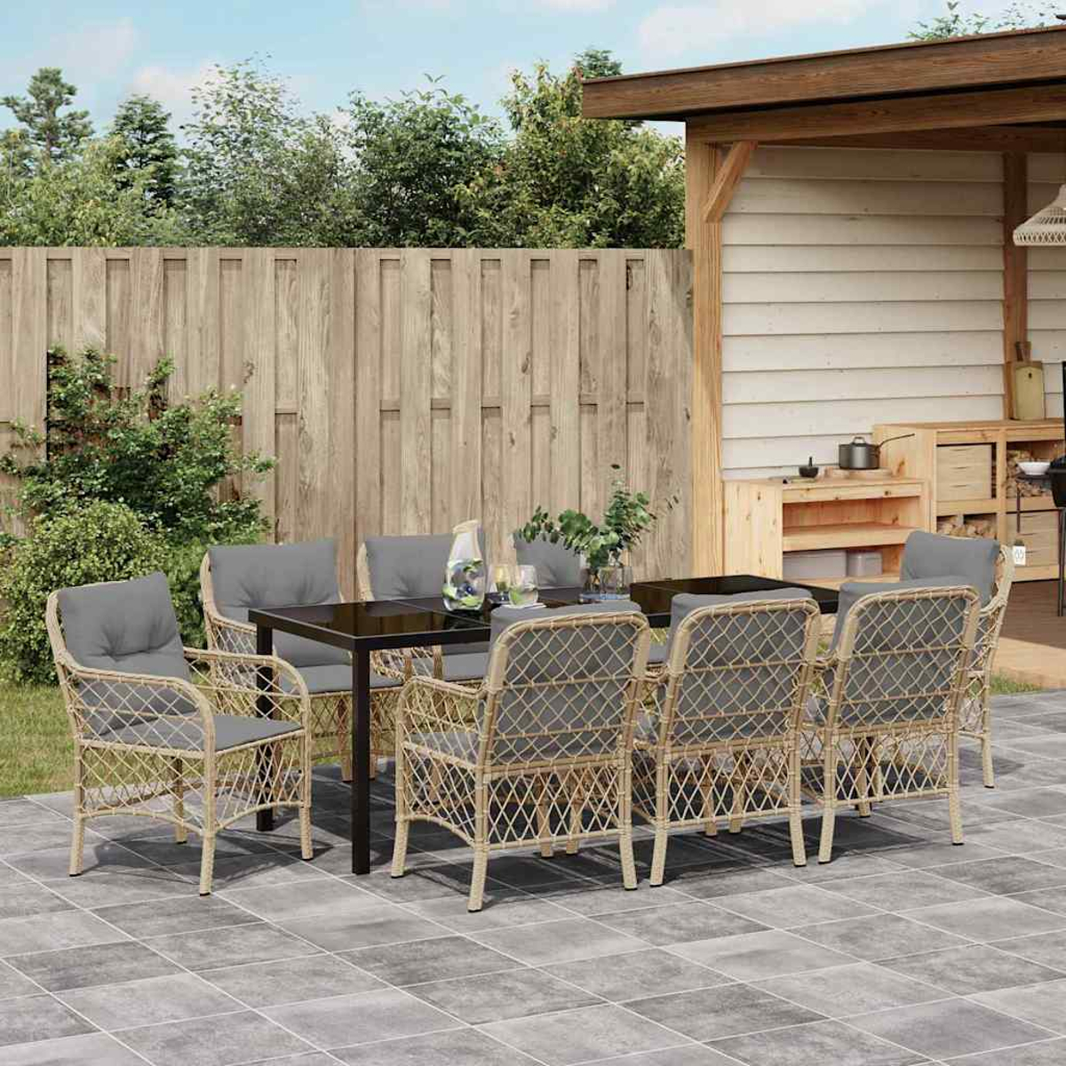 Essgruppe im Freien: Tisch und Stühle auf der Terrasse. Holzzaun und Schuppen im Hintergrund. Pflanzen und Laub vorhanden.