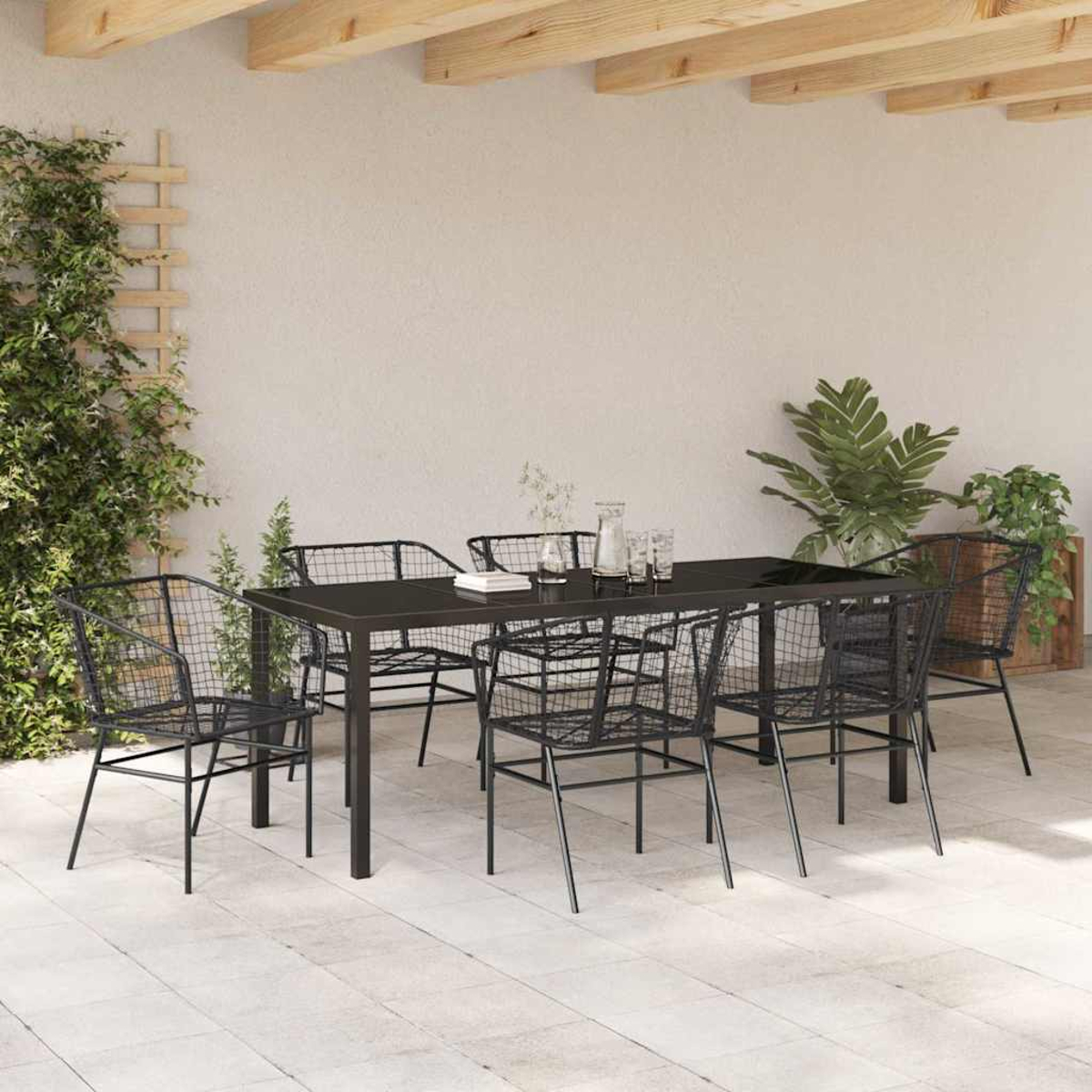Essgruppe im Freien: schwarzer Tisch, Drahtstühle, Pflanzen und Gläser auf einer Terrasse. Holzbalken oben, Kletterpflanzen an der Wand.
