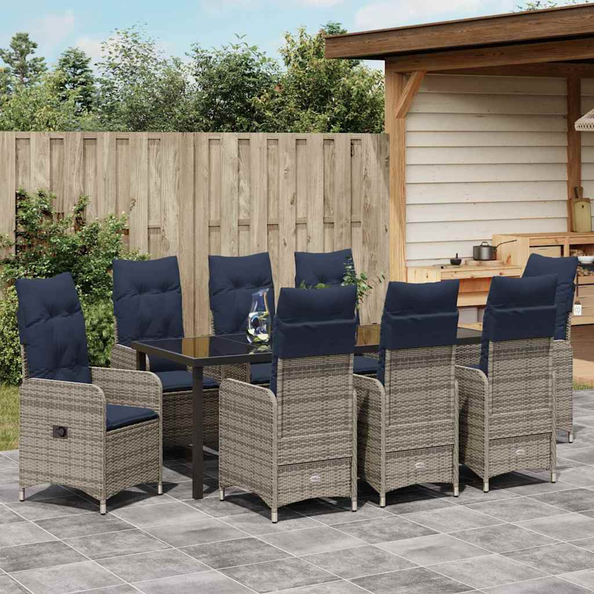 Essgruppe im Freien: Tisch, Stühle mit blauen Kissen, Holzzaun und Terrasse. Im Hintergrund ist eine überdachte Terrasse zu sehen.