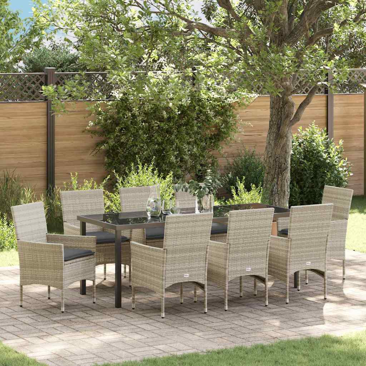 Essgruppe im Freien mit rechteckigem Tisch und acht Korbstühlen, auf einer Terrasse mit Holzzaun und Grün im Hintergrund.