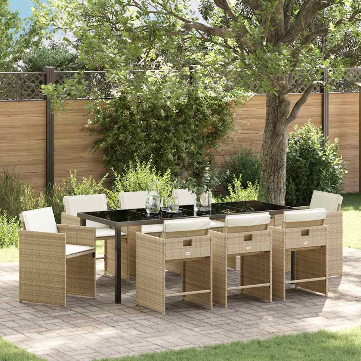 Set da pranzo all'aperto con tavolo nero e sedie in vimini su un patio in mattoni, circondato da alberi e una staccionata in legno.