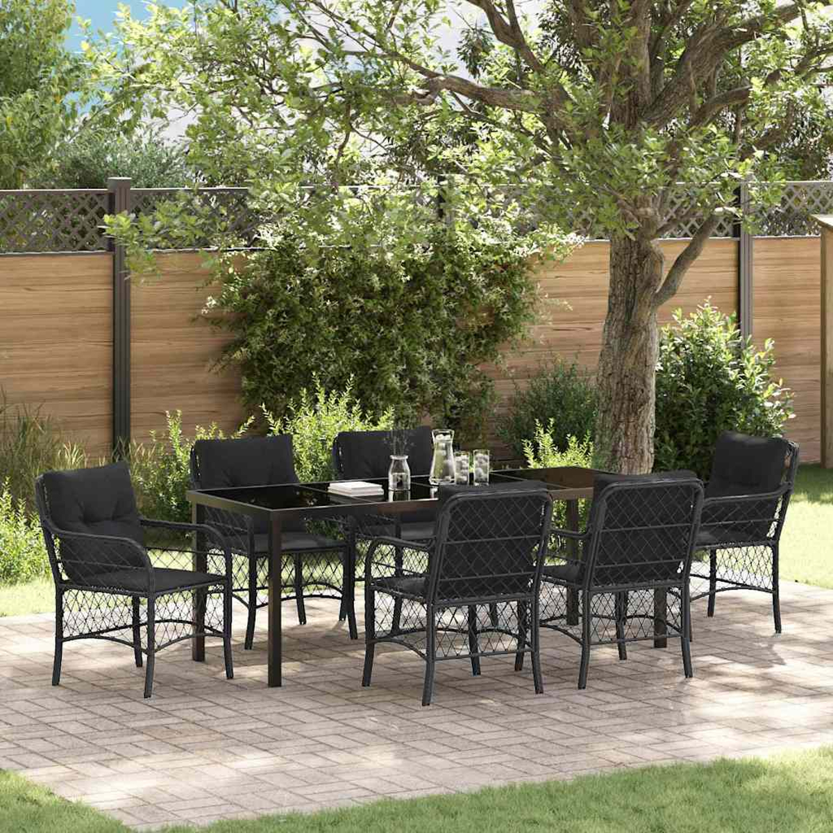 Essgruppe im Freien mit schwarzen Stühlen und Tisch. Auf einer Backstein-Terrasse mit Baum, Zaun und Grün im Hintergrund.