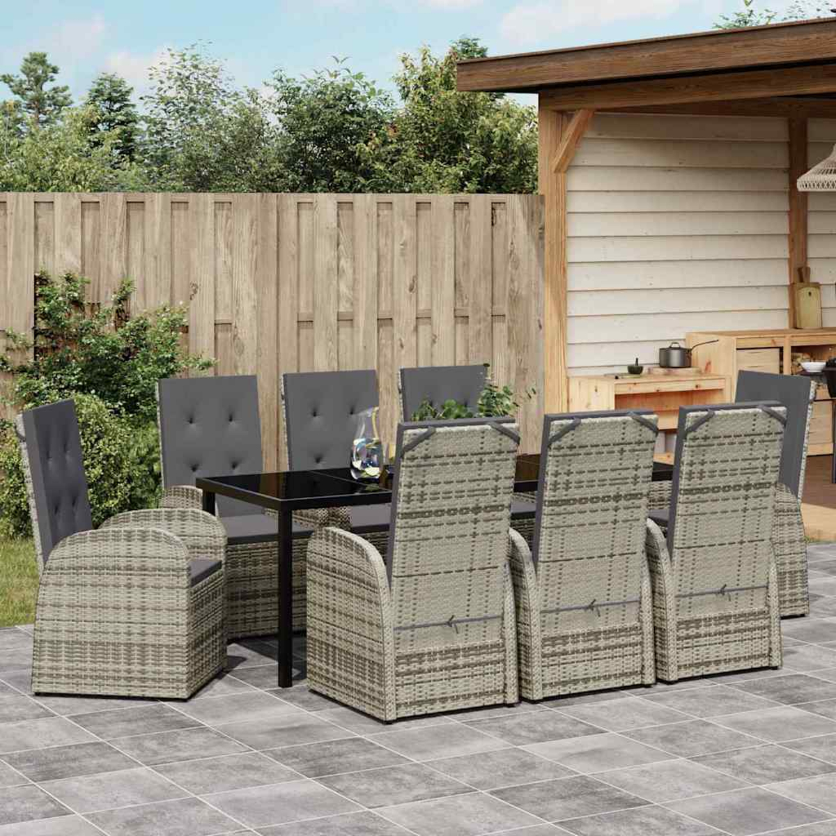 Essgruppe im Freien mit schwarzem Tisch, grau gepolsterten Stühlen, auf einer gefliesten Terrasse, mit Holzzaun und Schuppen im Hintergrund.