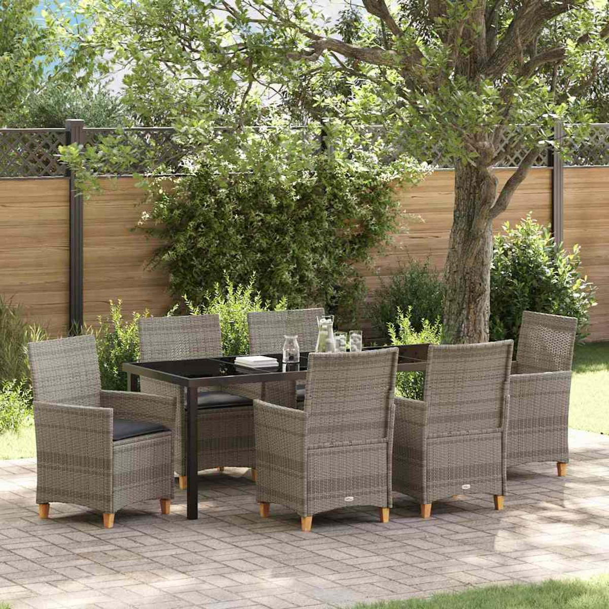 Terrassenset im Freien mit Tisch und sechs Stühlen. Im Hintergrund ein Baum und ein Holzzaun. Die Stühle sind aus grauem Korbgeflecht.