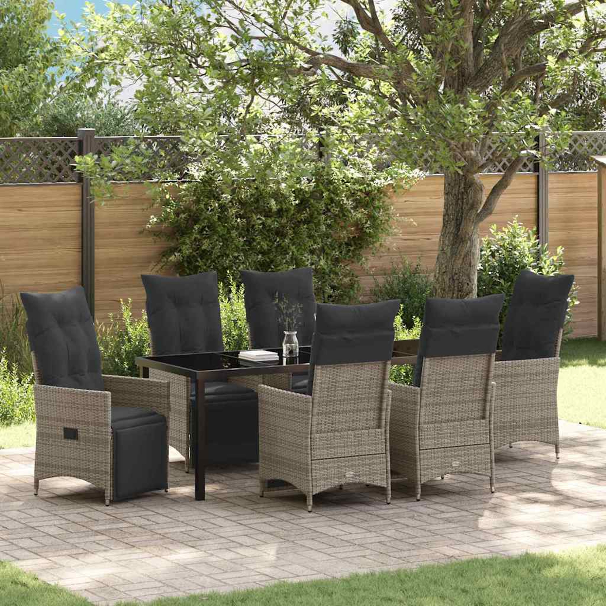 Essgruppe im Freien: Tisch mit Glasplatte und 6 Stühlen mit schwarzen Kissen auf einer Terrasse, umgeben von Bäumen und einem Holzzaun.