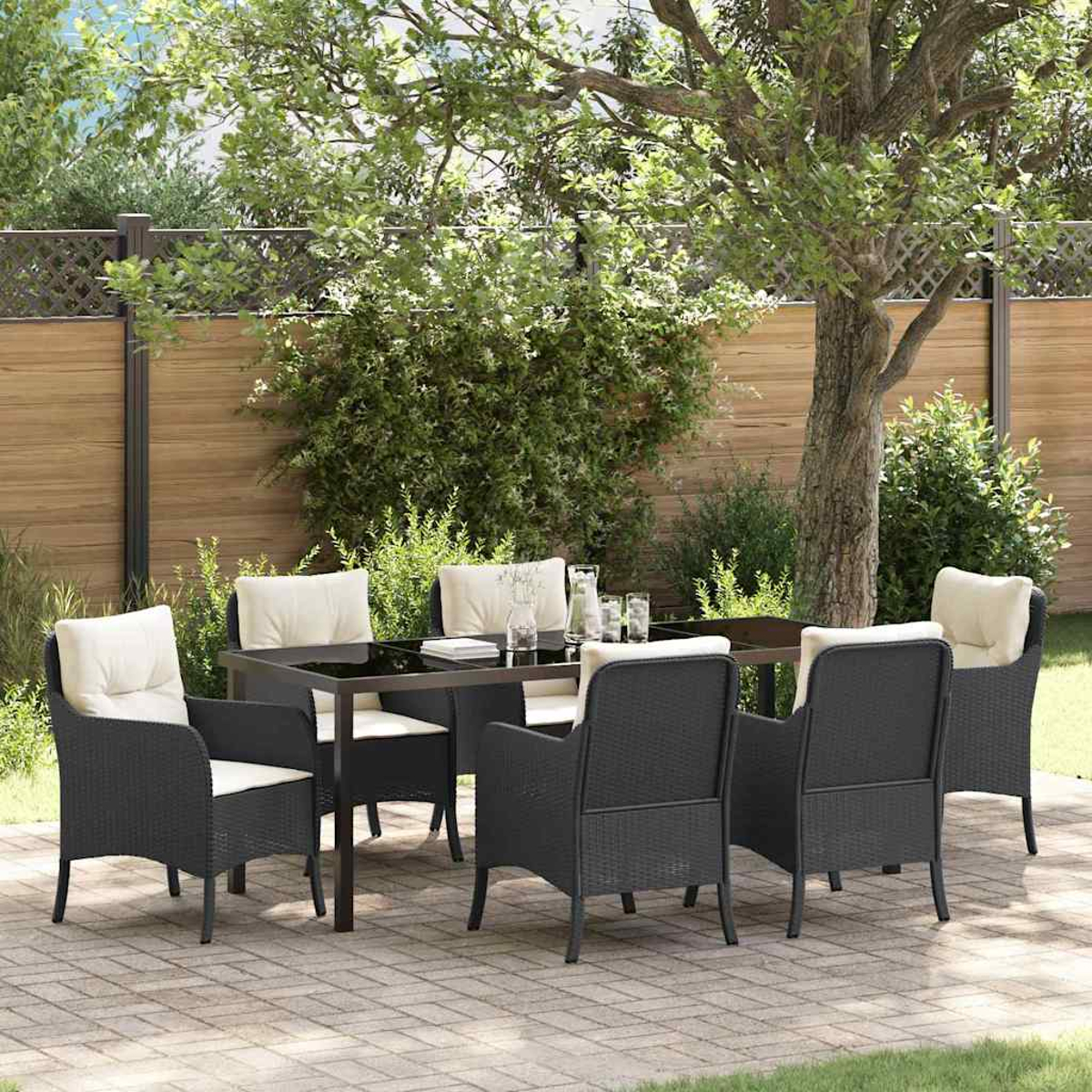 Essgruppe im Freien: schwarze Stühle mit cremefarbenen Kissen um einen Tisch, auf einer Ziegelterrasse, umgeben von Grün und einem Holzzaun.