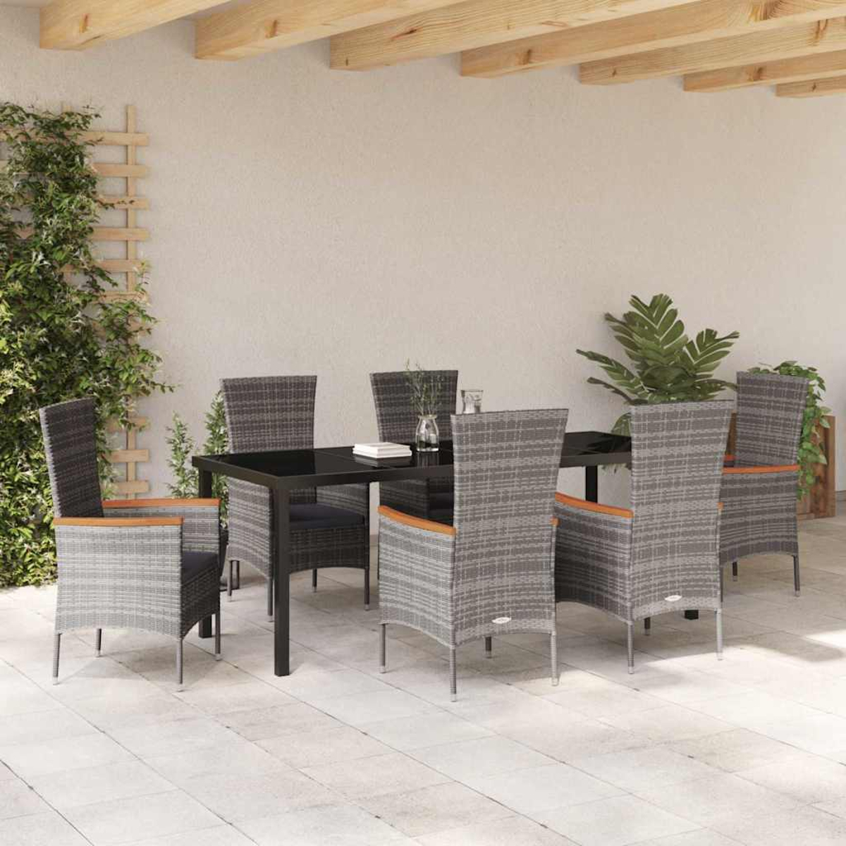 Essgruppe im Freien mit schwarzem Tisch und grauen Korbstühlen unter einer Holzpergola. Pflanzen und ein Spalier sind links.