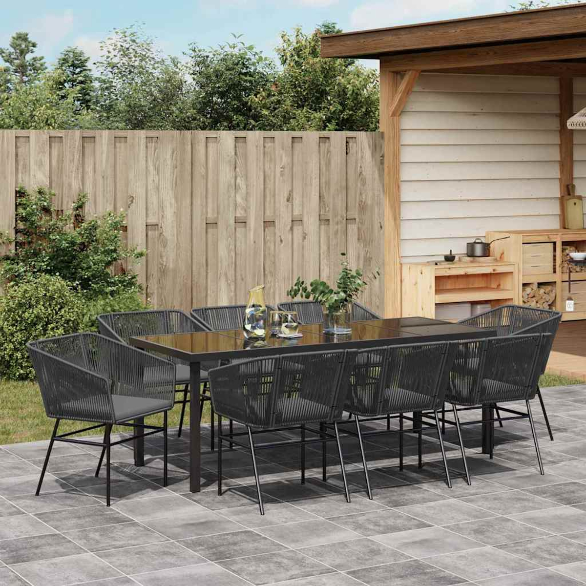 Essgruppe im Freien: Schwarzer Tisch, Stühle, Holzzaun, kleine Küchenzeile und Grün schaffen eine gemütliche Gartenszene.