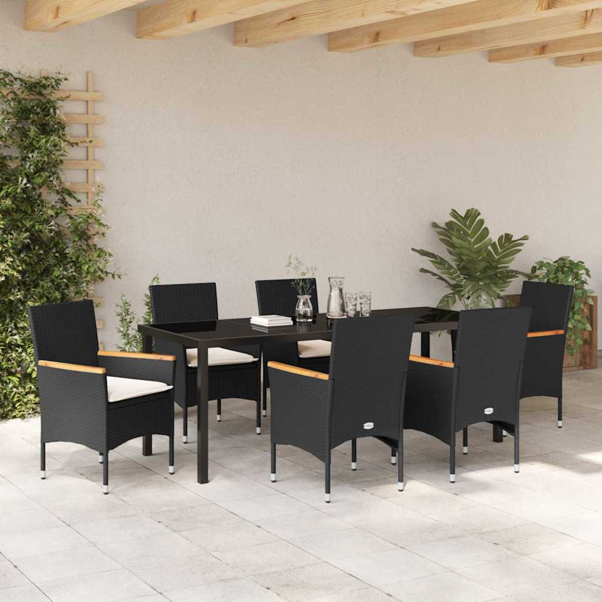 Eine Terrasse mit einem schwarzen Tisch und Stühlen. Pflanzen und Holzbalken sind im Hintergrund. Die Stühle haben helle Kissen.