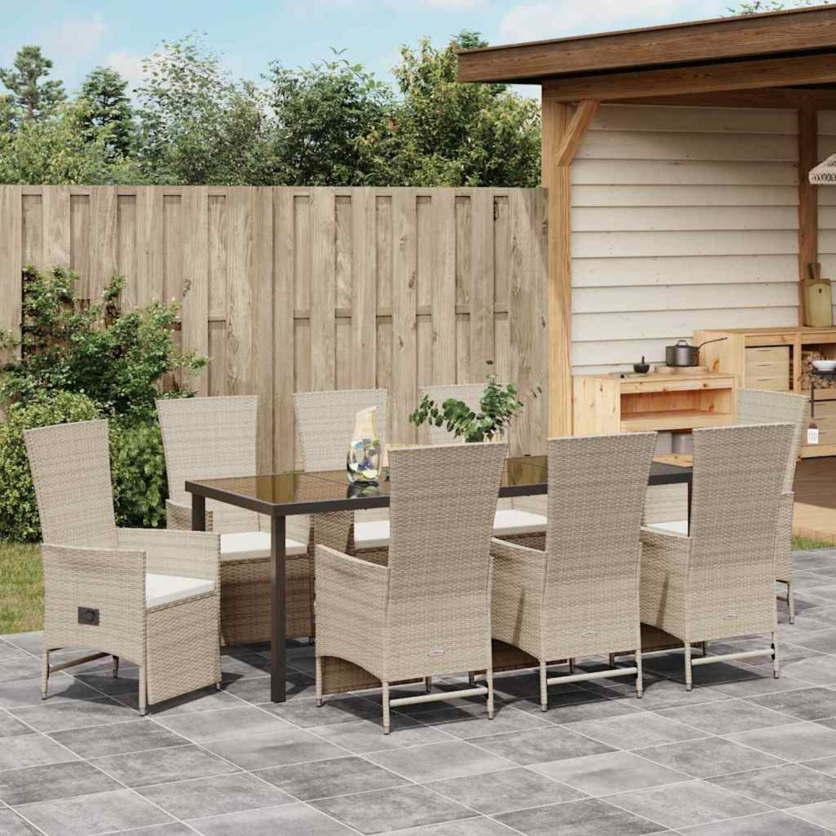 Essgruppe im Freien: Tisch mit Stühlen. Beige Korbstühle um einen dunklen Tisch. Holzzaun und Bäume im Hintergrund.