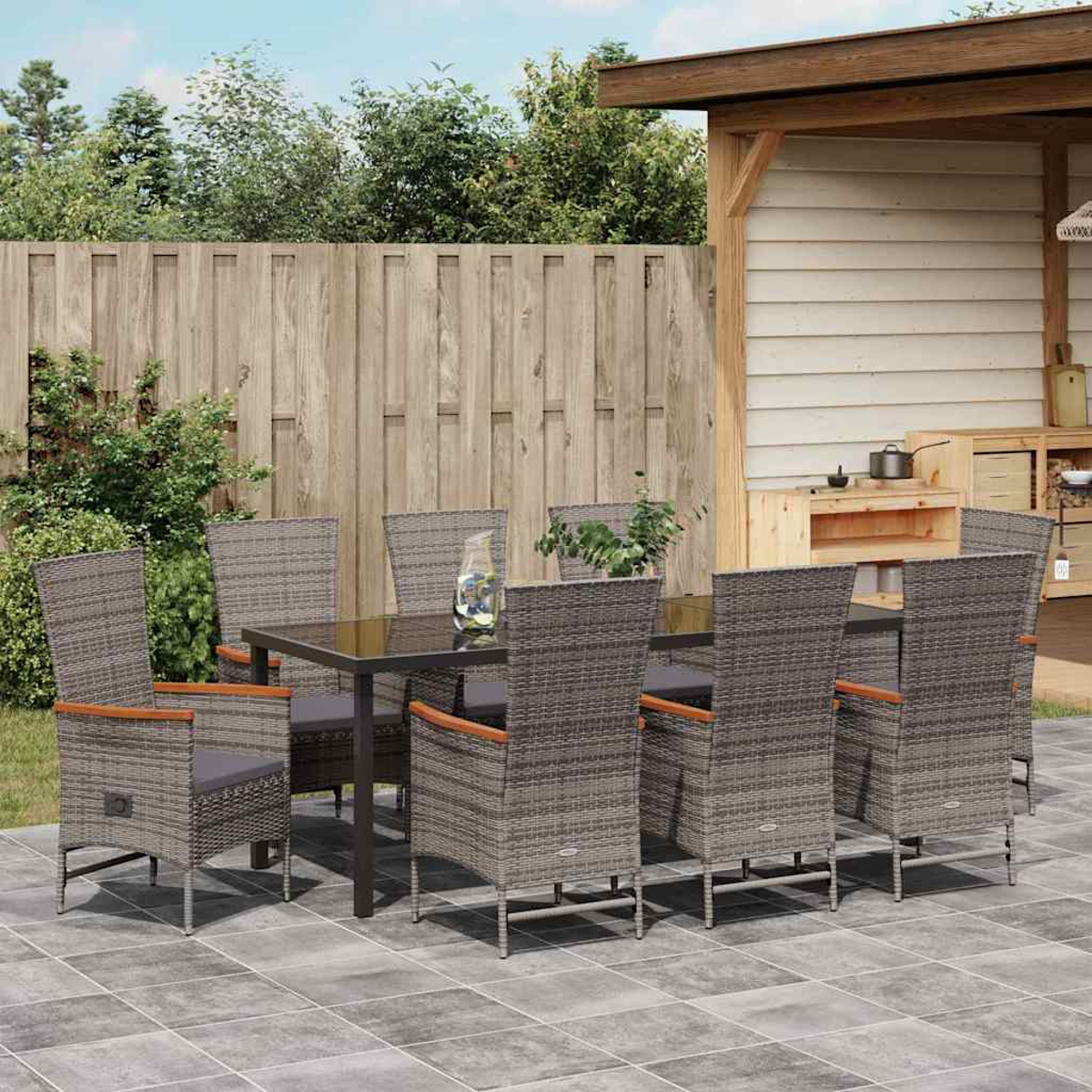 Essgruppe im Freien mit Tisch und Stühlen. Die Stühle sind aus grauem Korbgeflecht mit Holzarmlehnen auf einer gefliesten Terrasse.