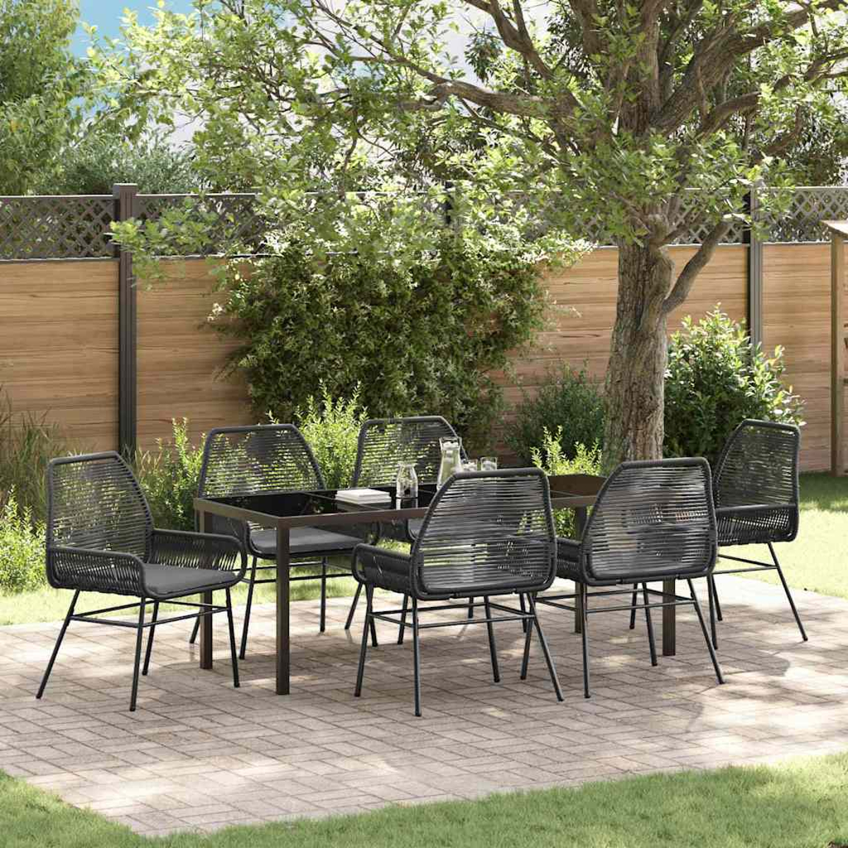 Eine Terrasse mit einem schwarzen Tisch und Stühlen. Im Hintergrund steht ein Baum. Die Terrasse besteht aus Ziegeln. Dahinter ist ein Zaun.