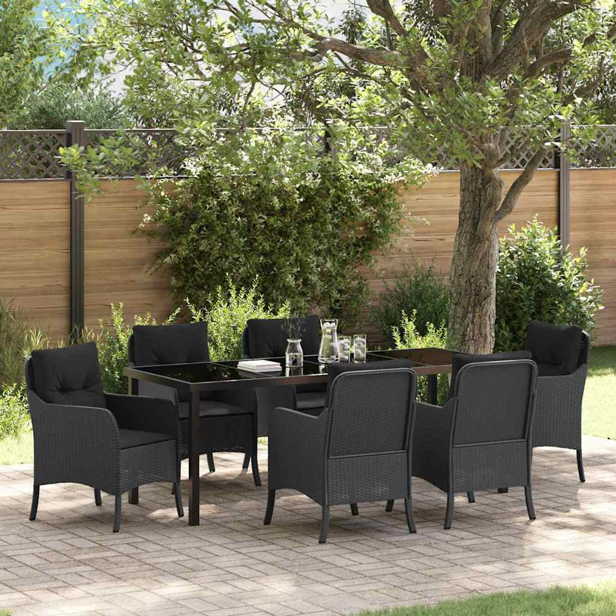 Gartengarnitur. Schwarzer Tisch und Stühle auf einer Terrasse mit Baum und Holzzaun im Hintergrund. Gläser und Krug.