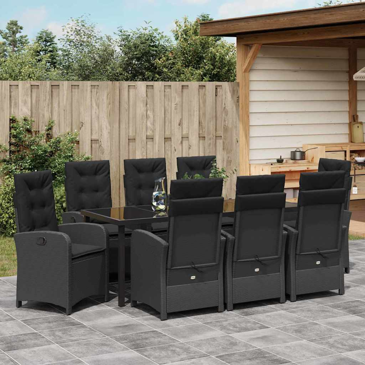 Essgruppe im Freien. Schwarze Stühle umgeben einen Tisch auf einer gefliesten Terrasse. Ein Holzzaun und ein Pavillon sind im Hintergrund.