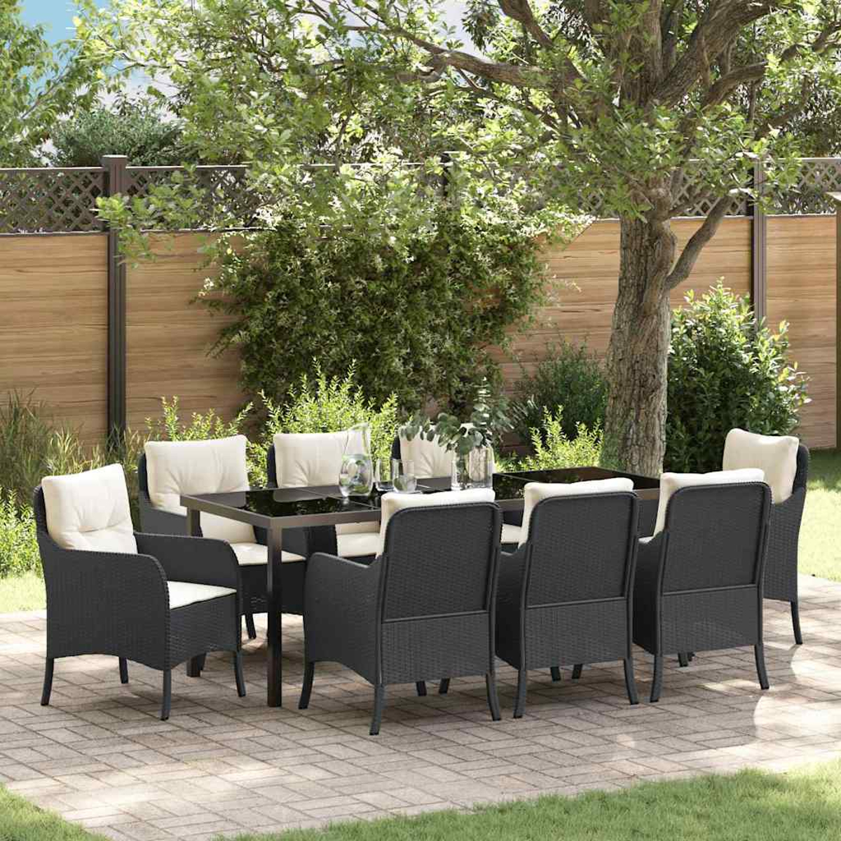 Essgruppe im Freien. Schwarze Korbstühle mit cremefarbenen Kissen umgeben einen schwarzen Tisch auf einer Terrasse. Grüne Bäume und ein Holzzaun sind im Hintergrund.