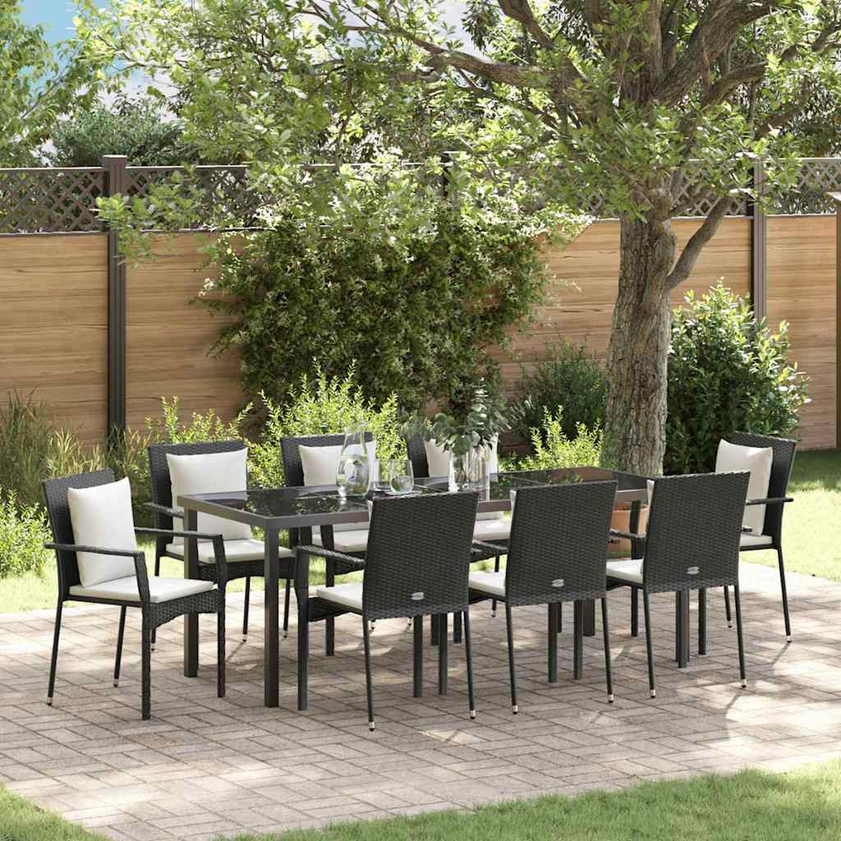 Essgruppe im Freien. Schwarze Korbstühle mit weißen Kissen umgeben einen schwarzen Tisch. Die Szene spielt auf einer Terrasse mit Holzzaun.
