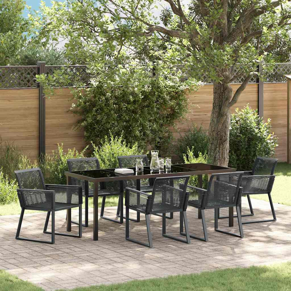 Essgruppe im Freien mit einem schwarzen Glastisch und grauen Stühlen. Ein Baum beschattet die Terrasse. Im Hintergrund ist ein Holzzaun zu sehen.