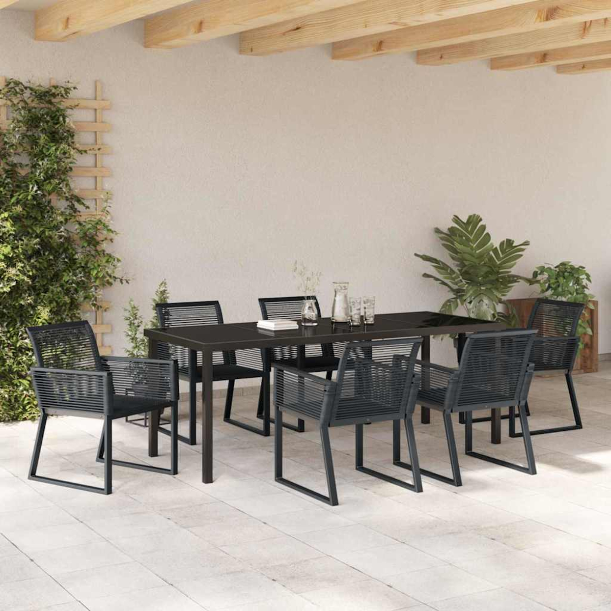 Essgruppe im Freien: schwarzer Tisch und Stühle. Pflanzen im Hintergrund. Holzbalken oben. Gepflasterte Terrasse.