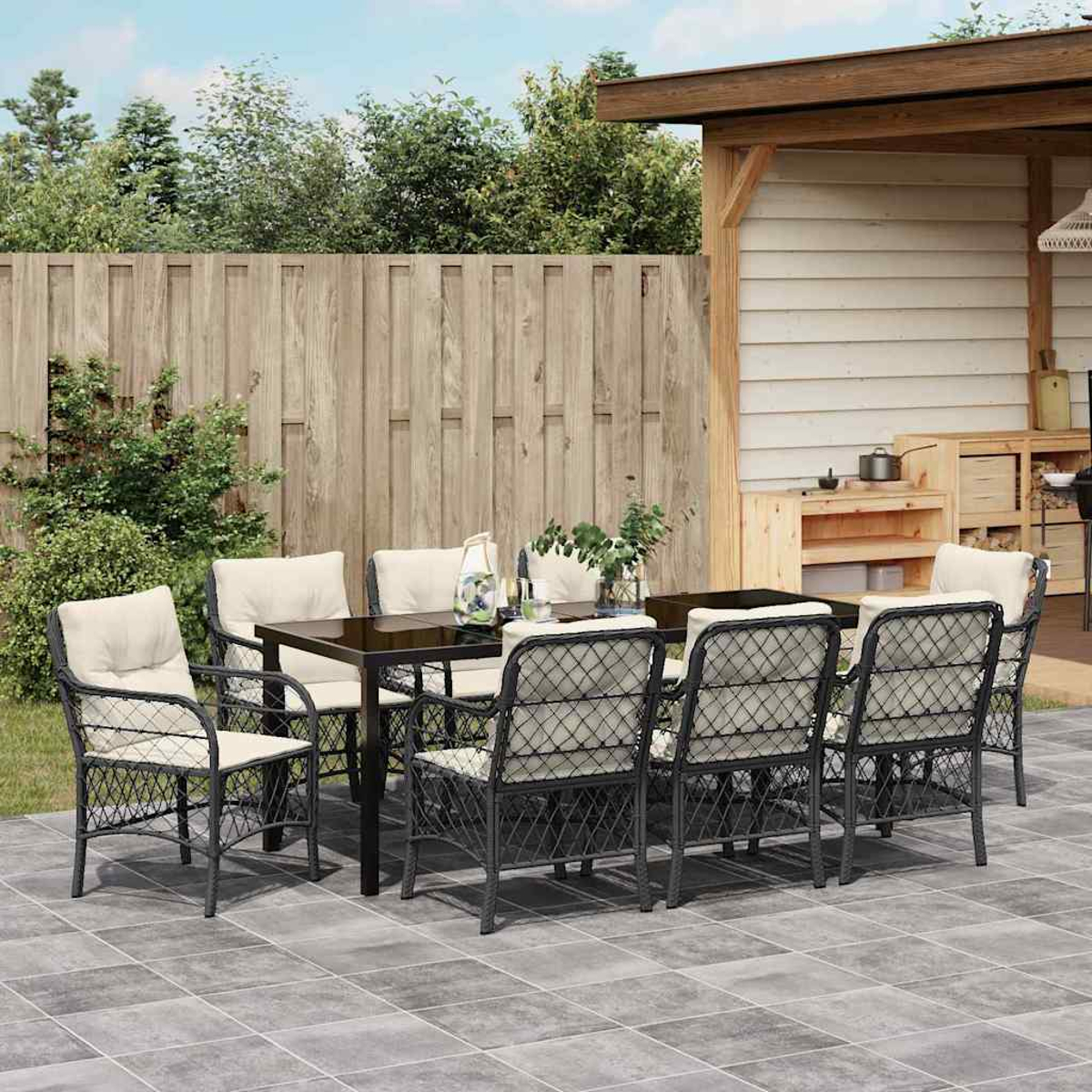Essgruppe im Freien auf einer Terrasse. Enthält einen Tisch, Stühle und einen Holzzaun im Hintergrund. Ein Sonnenschirm ist ebenfalls sichtbar.