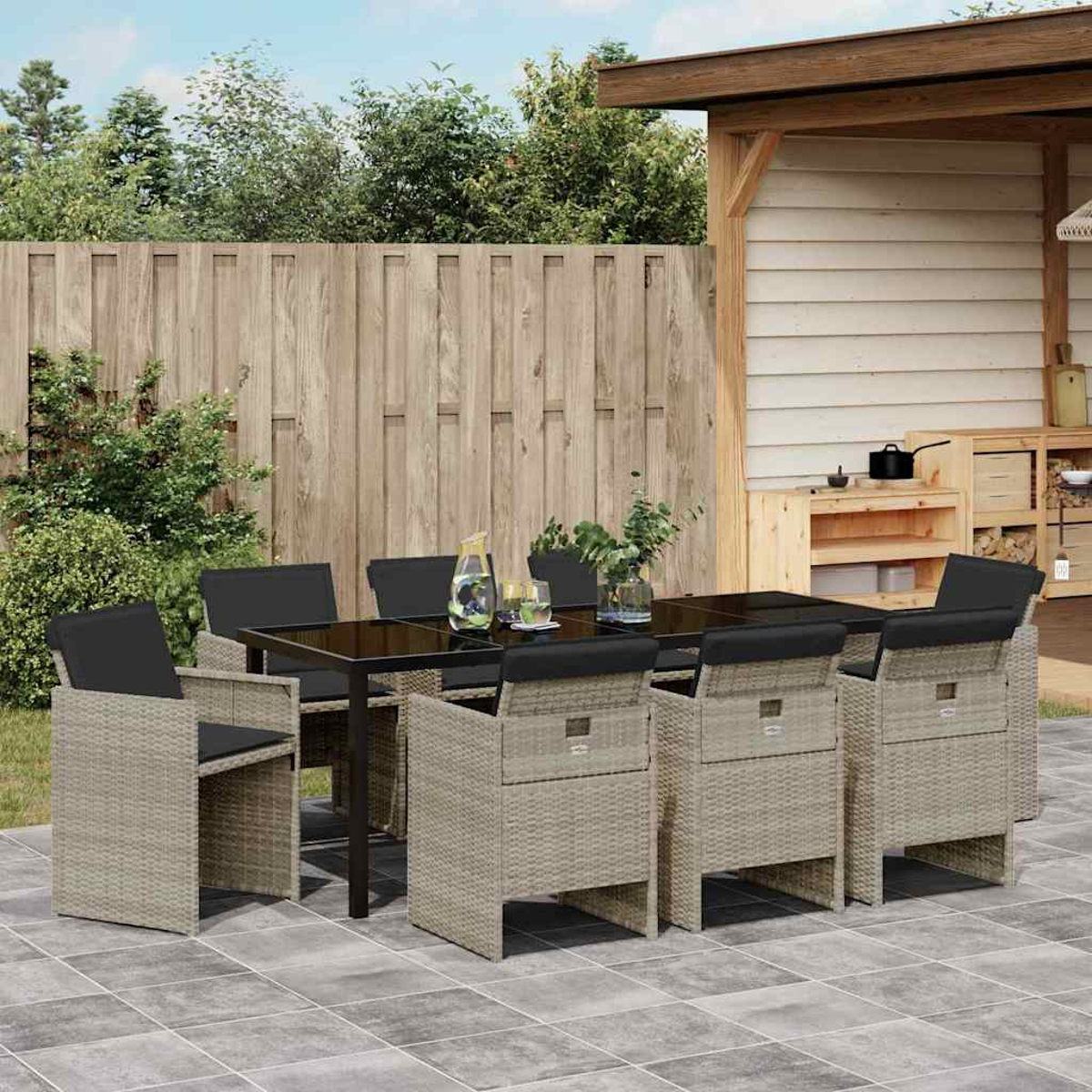 Essgruppe im Freien auf einer Terrasse. Enthält einen Tisch mit schwarzer Platte, Korbstühle und einen Holzzaun im Hintergrund.