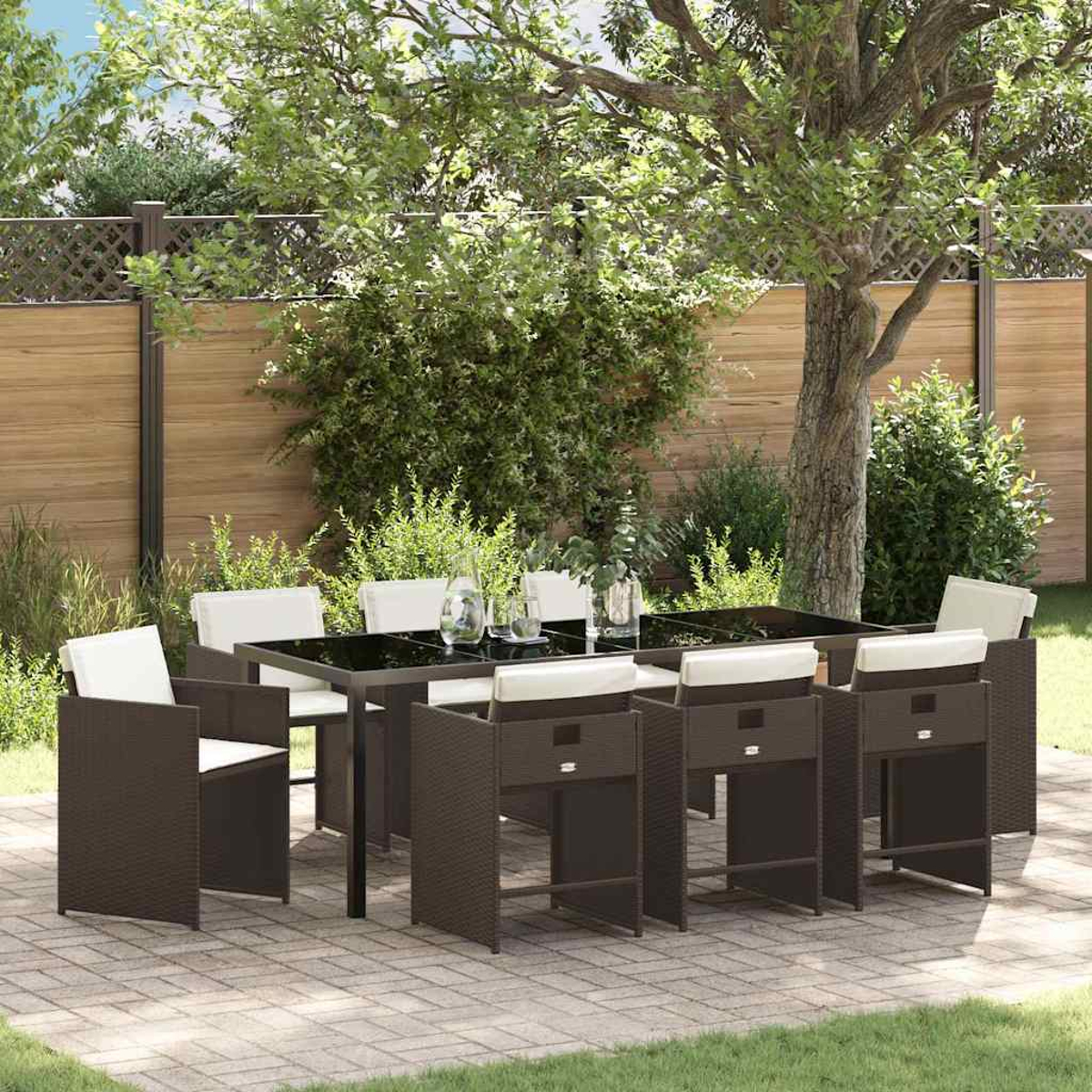 Essgruppe im Freien. Braune Korbstühle und Tisch mit schwarzer Platte, weiße Kissen, auf einer Terrasse mit Holzzaun und Grün.