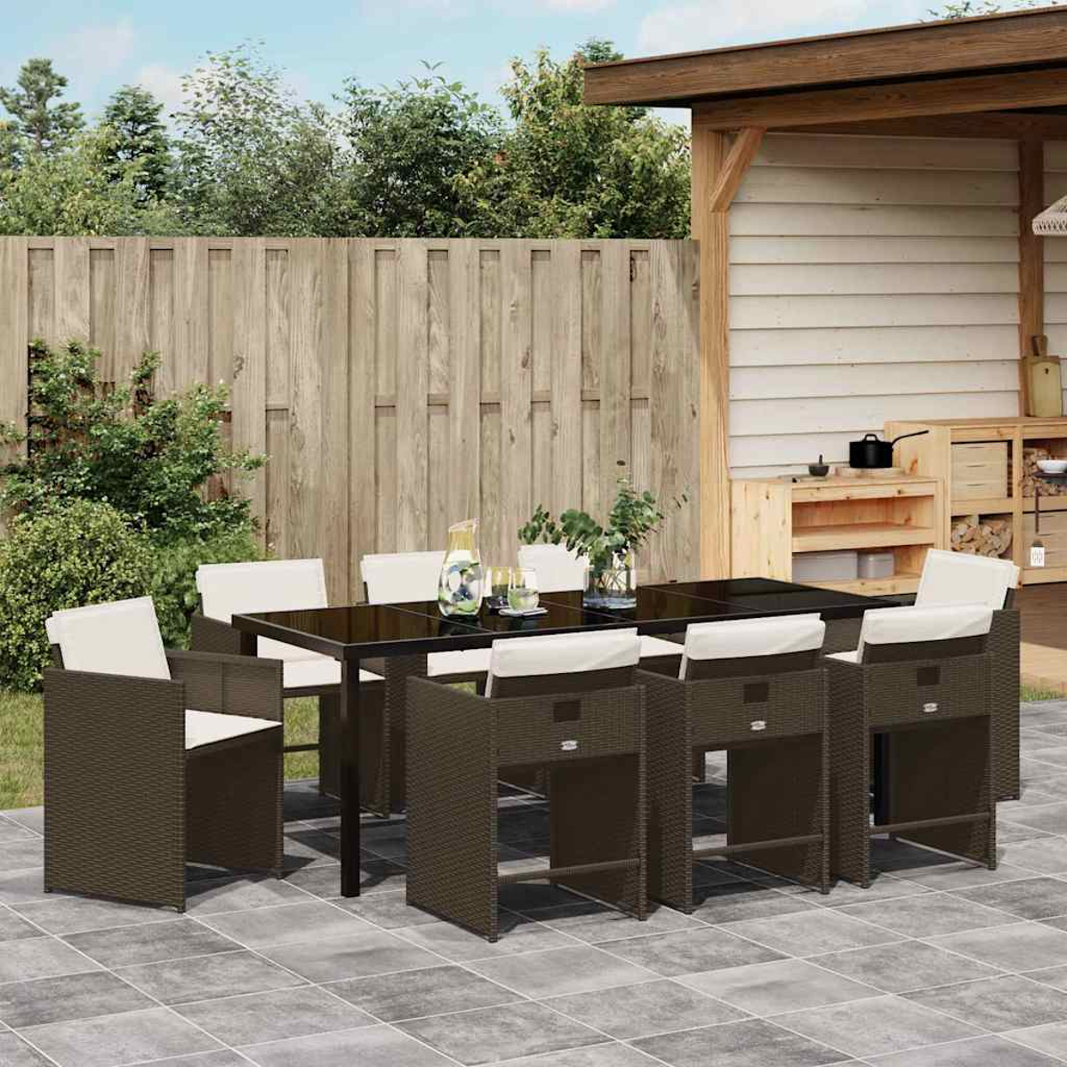 Essgruppe im Freien mit schwarzem Tisch, braunen Stühlen mit weißen Kissen und Holzzaun im Hintergrund.