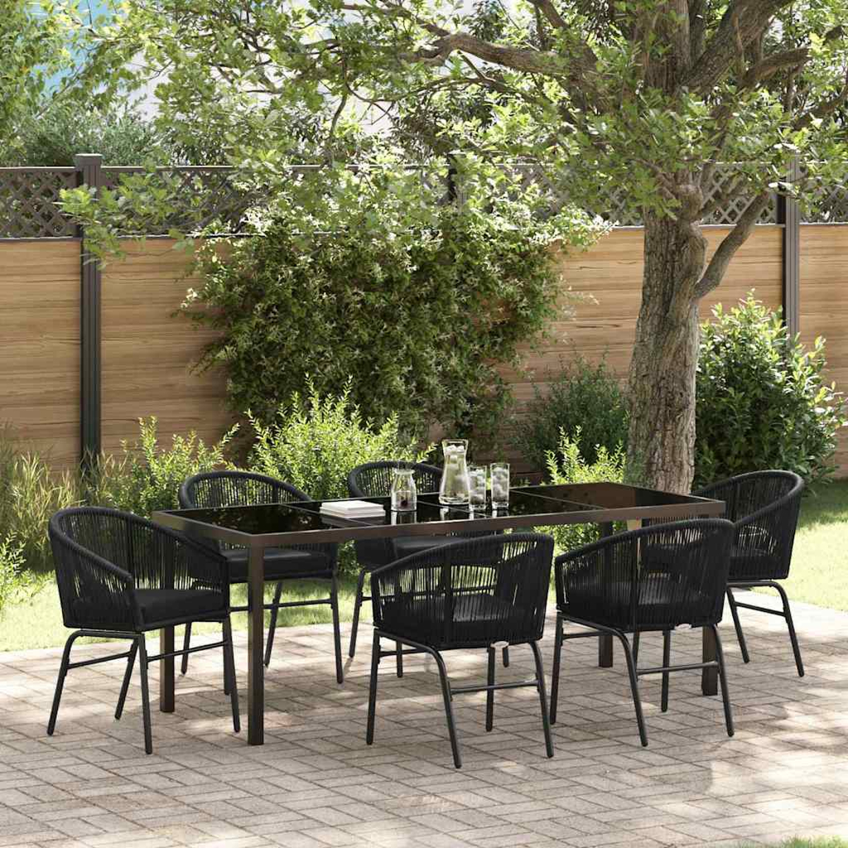 Eine Terrasse mit einem schwarzen Tisch und sechs Stühlen. Krug und Gläser auf dem Tisch. Bäume und ein Holzzaun im Hintergrund.