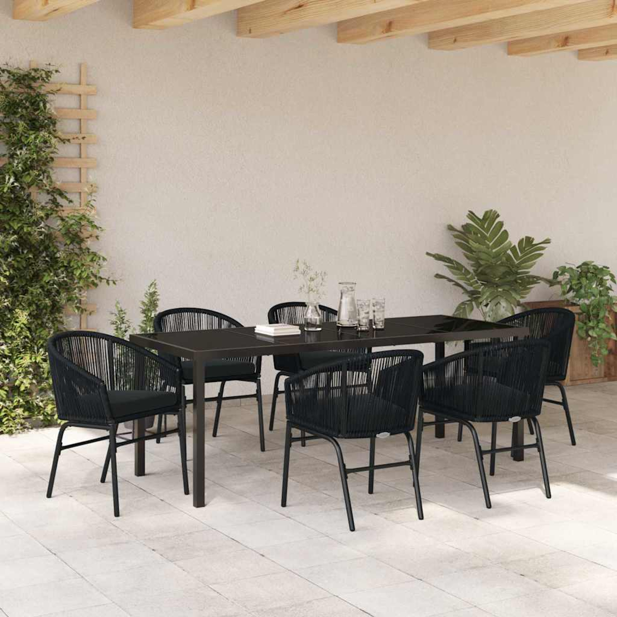 Terrassengarnitur mit schwarzem Tisch und Stühlen. Pflanzen und ein Spalier sind links. Weiße Wand im Hintergrund.