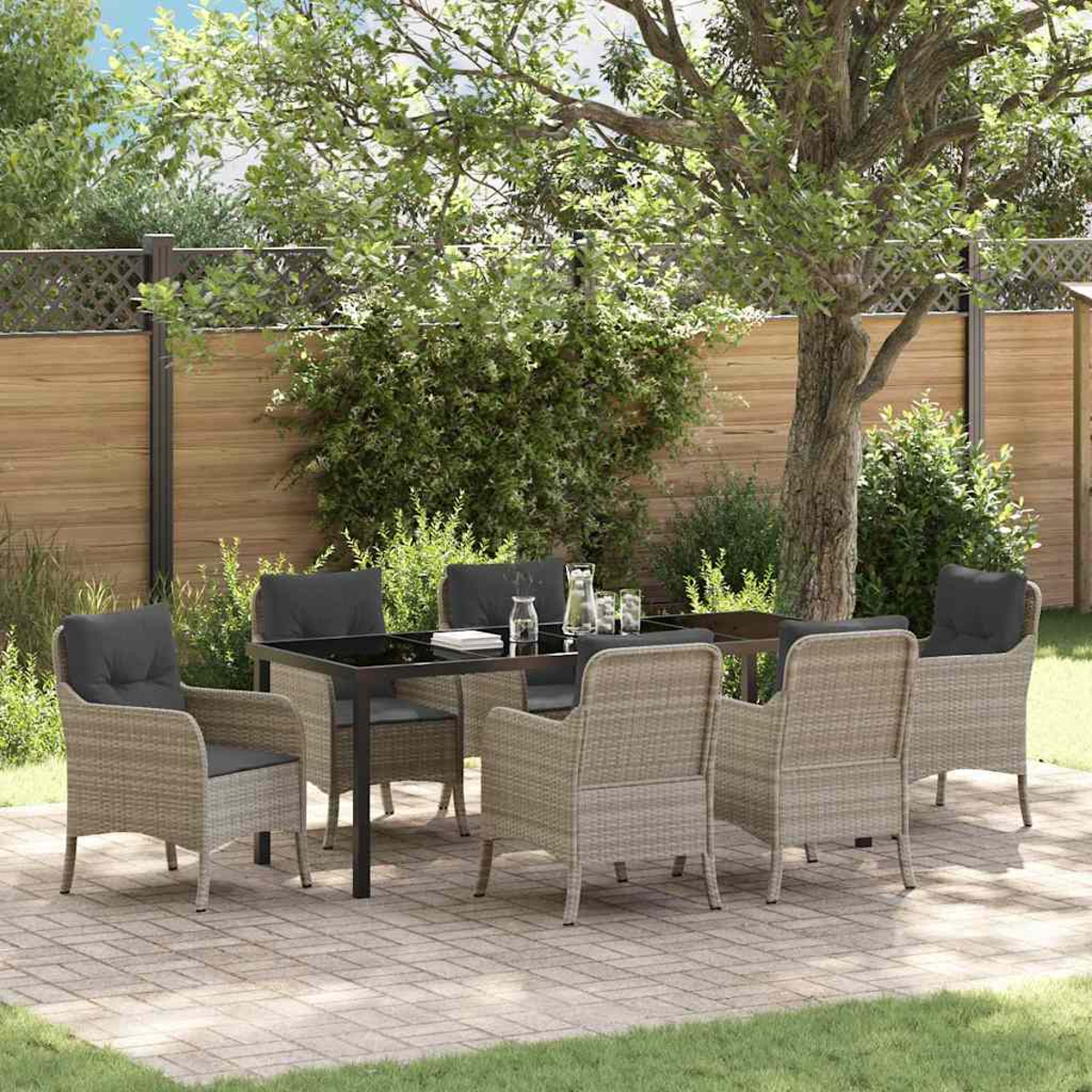 Eine Terrasse mit Tisch und Stühlen. Im Hintergrund sind ein Holzzaun und grüne Bäume zu sehen. Die Stühle haben graue Kissen.