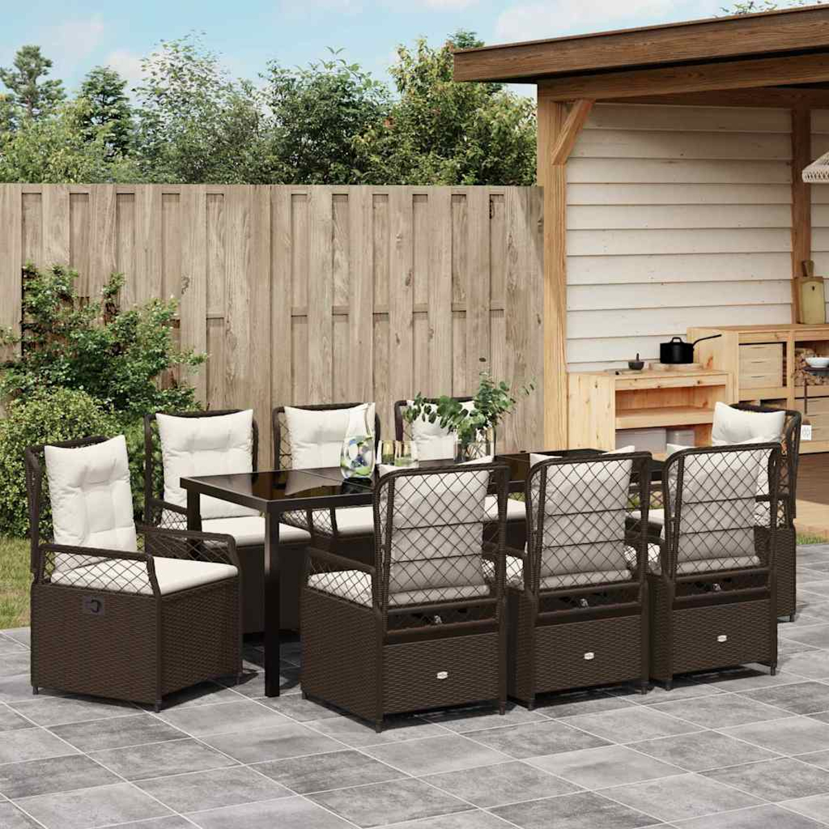Terrassenset: braune Korbstühle mit weißen Kissen um einen Tisch. Holzzaun und Schuppen im Hintergrund.