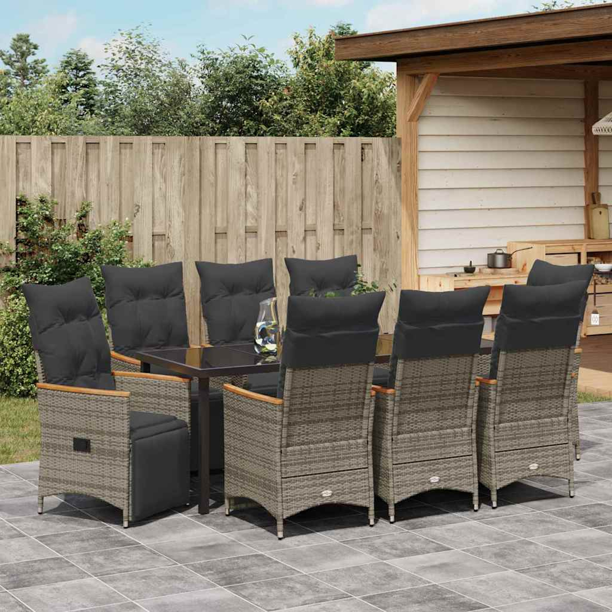 Essgruppe im Freien: ein Tisch mit Glasplatte und sechs Stühlen mit grauen Kissen, auf einer gefliesten Terrasse, Zaun und Grün im Hintergrund.