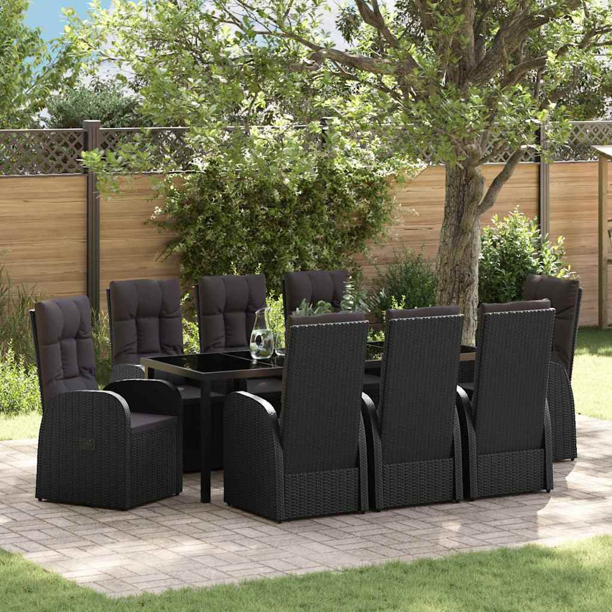 Ein schwarzes Ess-Set aus Korbgeflecht steht auf einer Ziegelterrasse. Enthält einen Tisch, Stühle und eine Wasserkaraffe aus Glas. Bäume und ein Zaun sind dahinter.