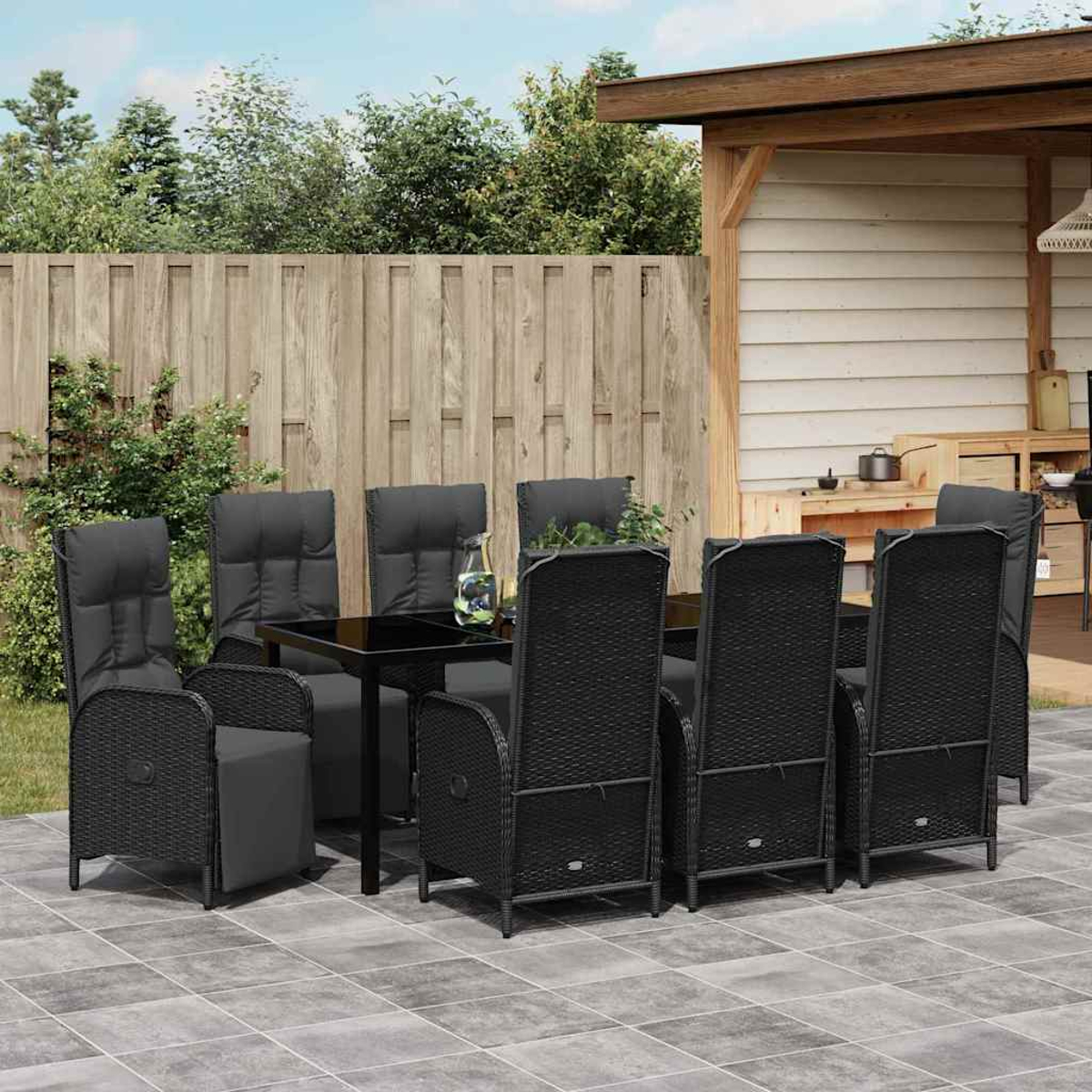 Essgruppe im Freien: schwarzer Tisch und Stühle auf einer gefliesten Terrasse. Im Hintergrund ein Holzzaun und ein überdachter Kochbereich.