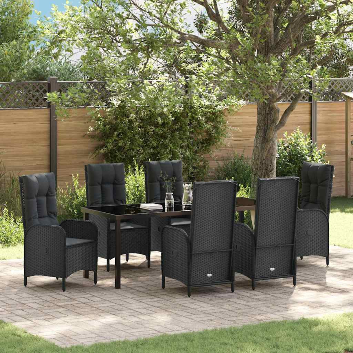 Eine Terrasse mit schwarzem Tisch und Stühlen. Im Hintergrund ein Holzzaun, üppiges Grün und ein großer Baum.