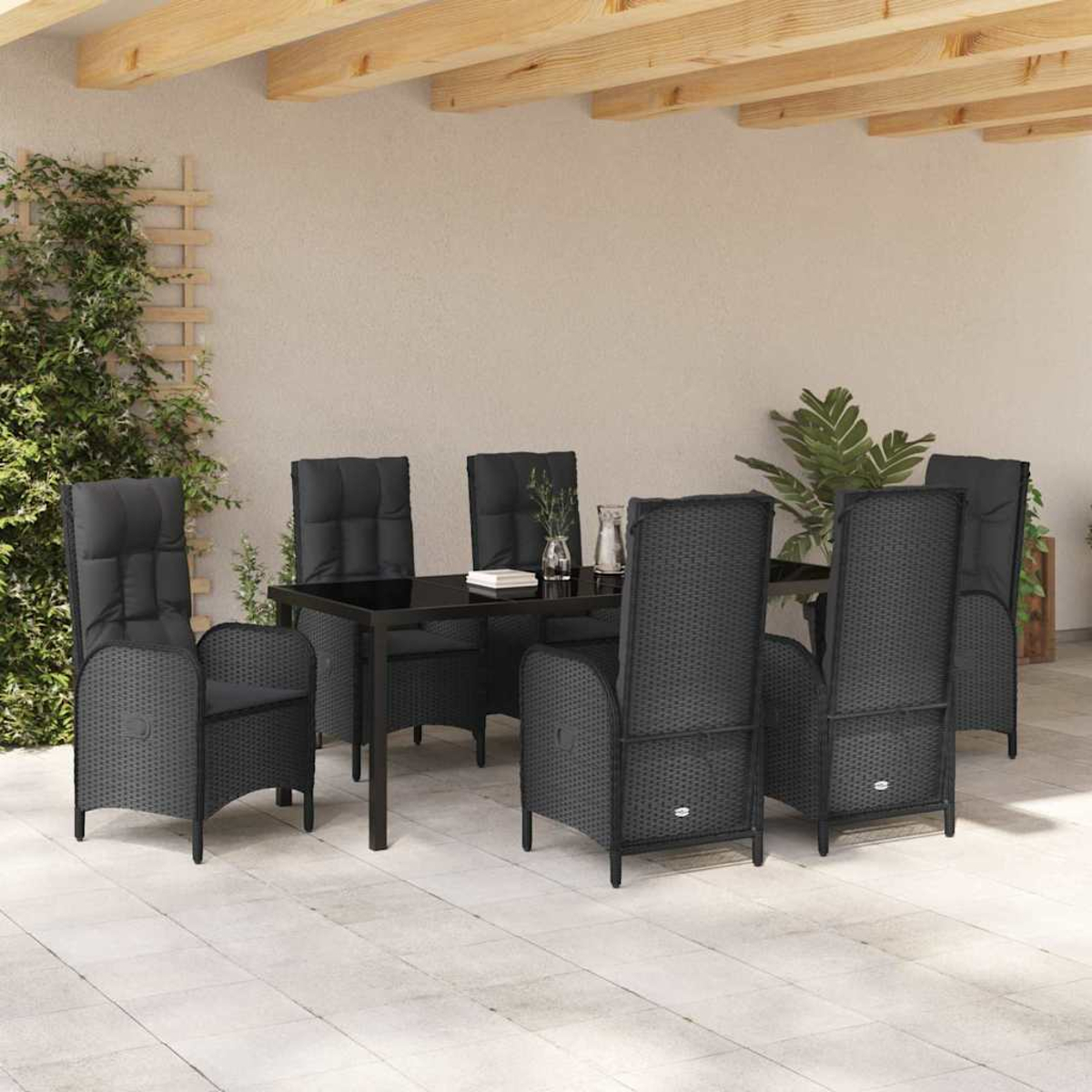 Garten-Terrassenset mit schwarzen Korbstühlen und einem Tisch. Pflanzen und Holzbalken im Hintergrund. Gepflasterter Terrassenboden.
