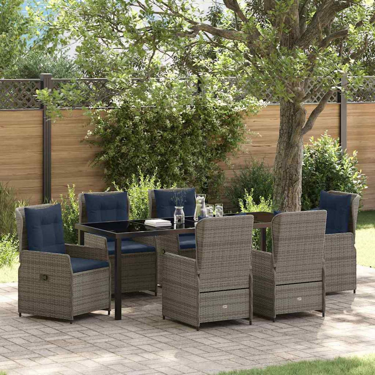 Essgruppe im Freien. Rattan-Stühle mit blauen Kissen umgeben einen Tisch mit Glasplatte. Ein Baum und Holzzaun im Hintergrund.